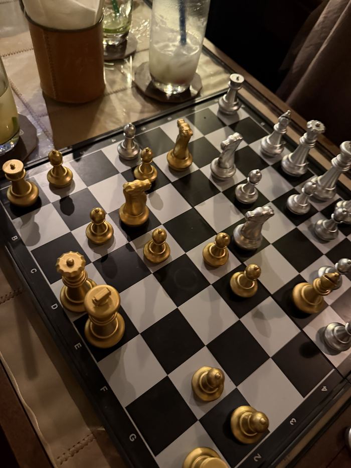 A gold and silver chess set mid-game on a cafe table