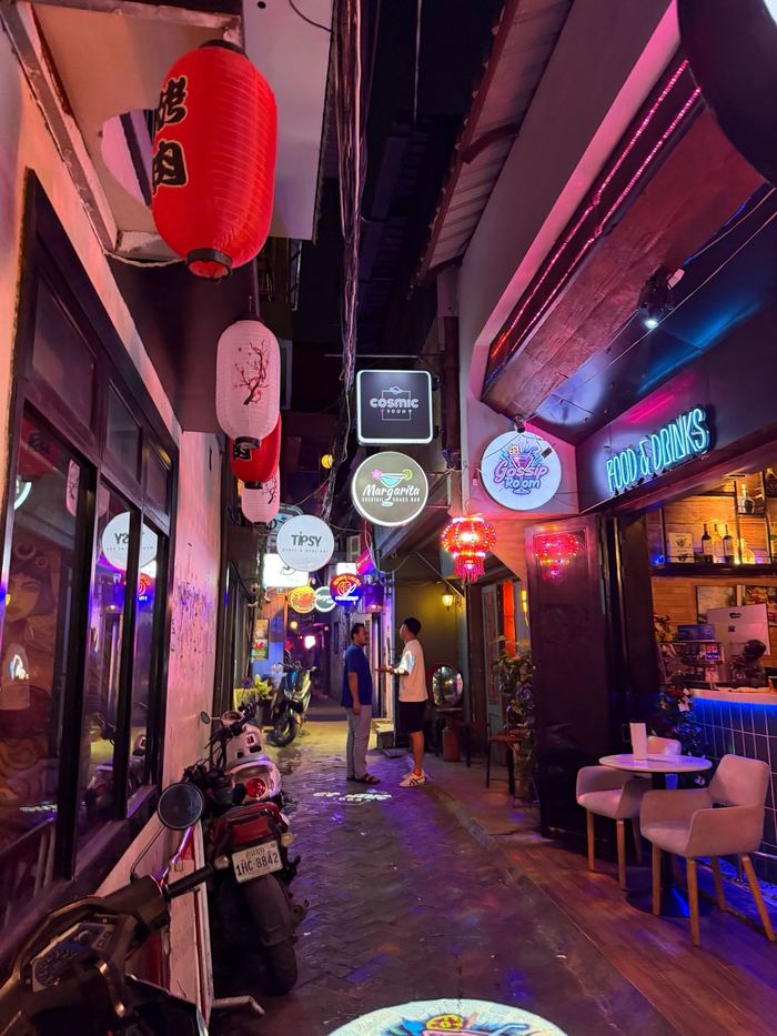 A narrow alley lit with neon signs and red lanterns at night