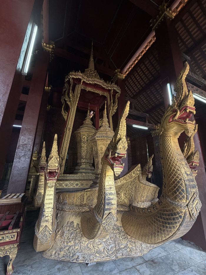 A gilded carriage decorated with naga serpent heads inside a temple hall