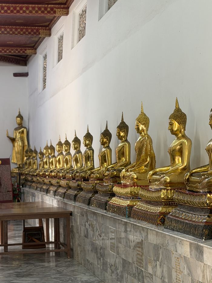 A long row of seated golden Buddha statues along a white wall