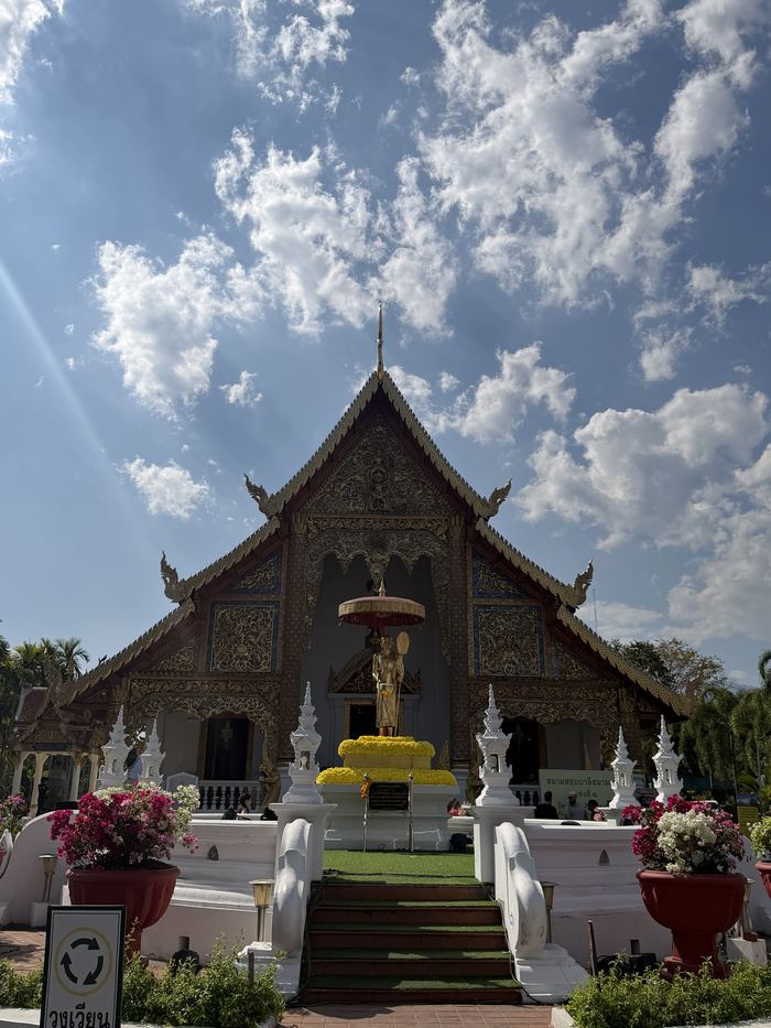 A white and gold temple hall with a golden statue out front