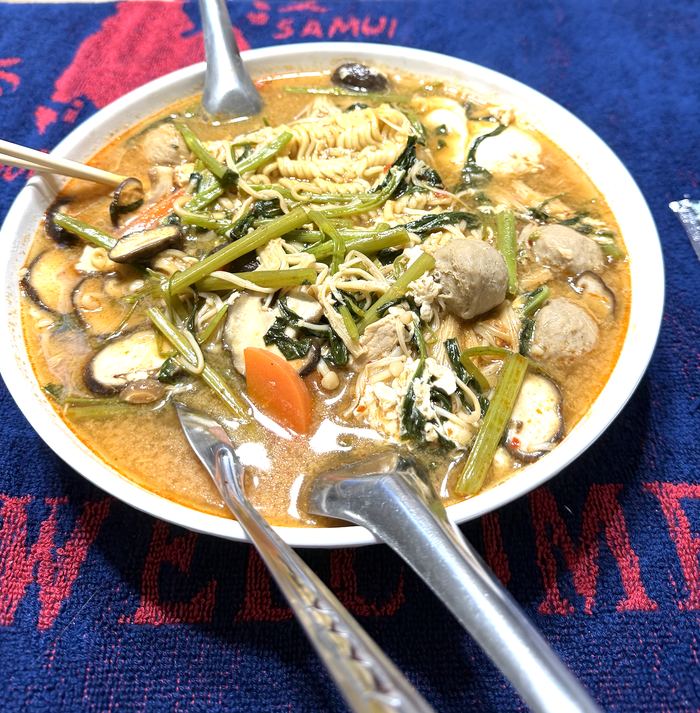 A bowl of noodle soup with greens, mushrooms, and meatballs