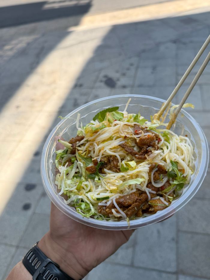 A cup of mixed noodles held over the sidewalk