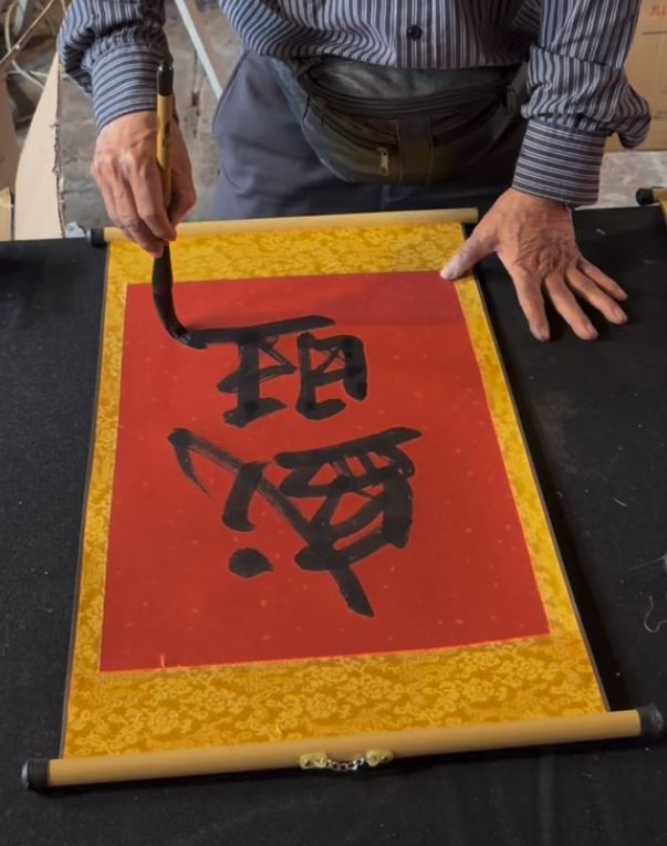 A calligrapher painting Vietnamese characters on a red scroll