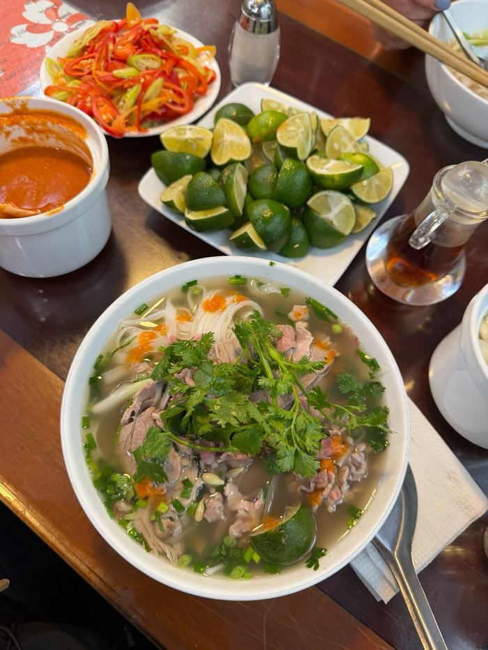 A bowl of pho with lime and chili on the side