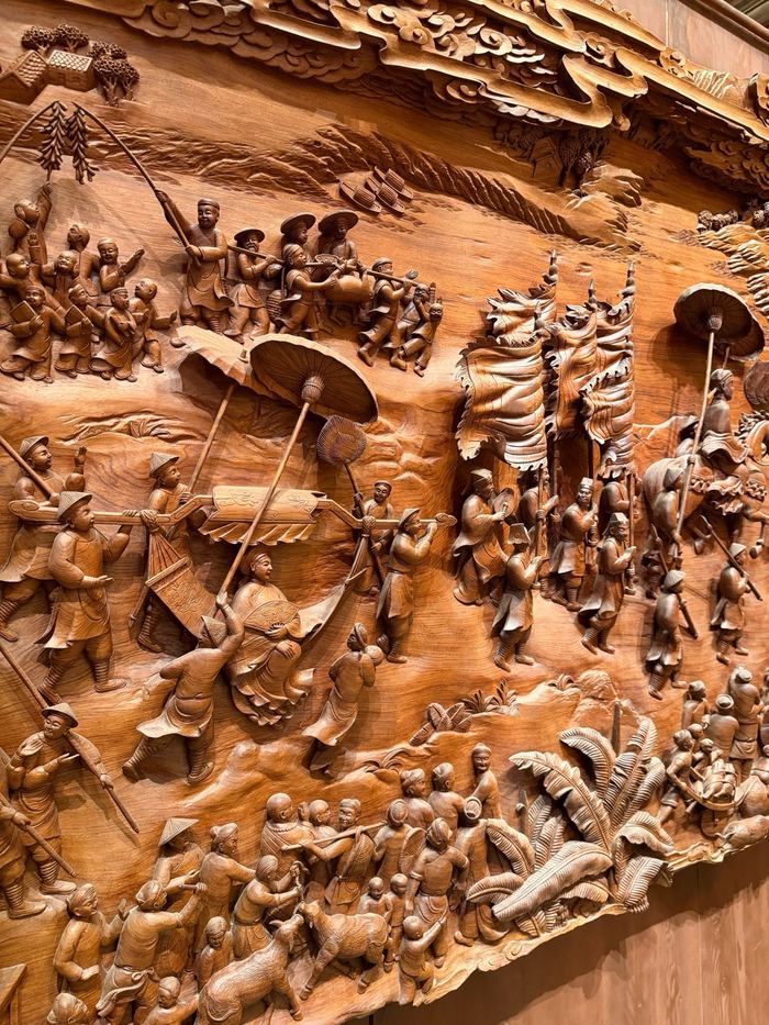 A detailed wooden relief carving of a crowded village scene