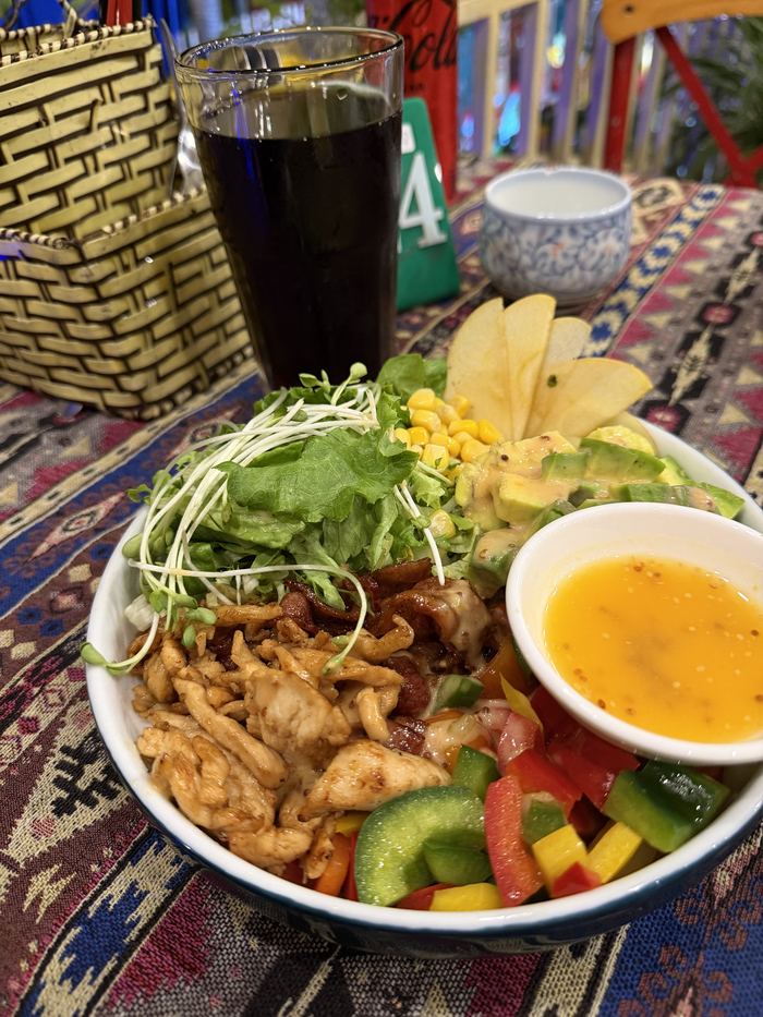 A chicken salad bowl with dressing and a cola