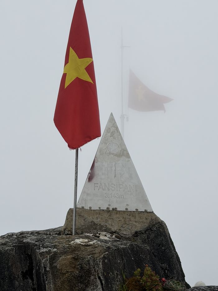The Fansipan summit marker and a Vietnamese flag in thick fog